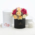 Vibrant pink, peach, and cream roses in black box with gold logo, beside white candle and heart card.