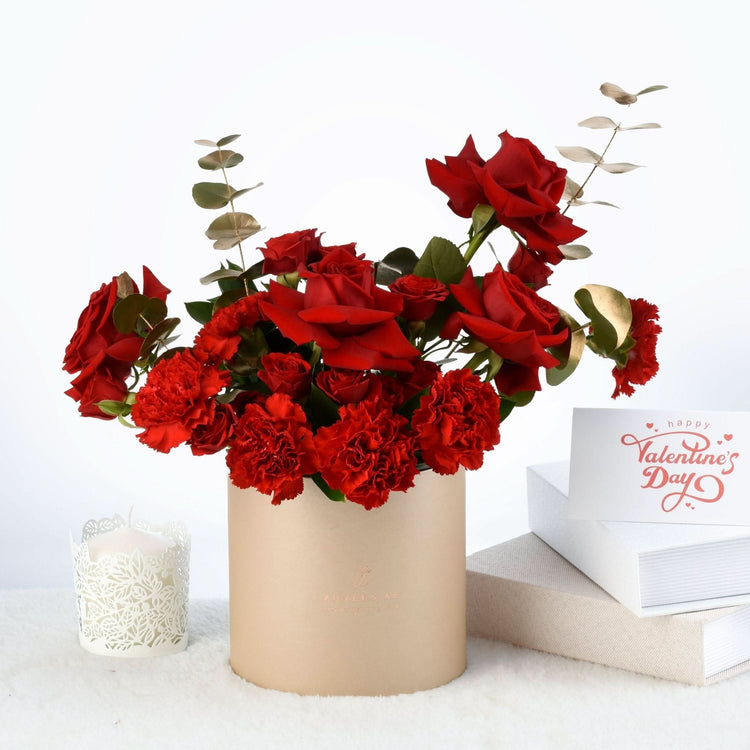 Vibrant red roses and carnations in beige cylinder vase, beside Valentine&