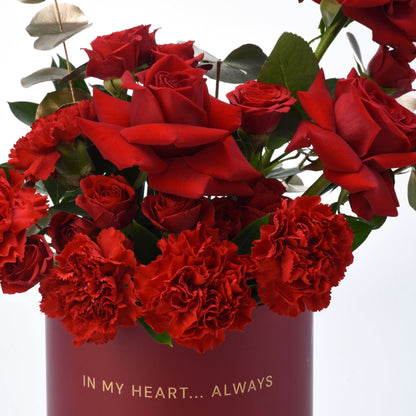 Vibrant red roses and carnations in deep burgundy vase with gold "In My Heart... Always" text.
