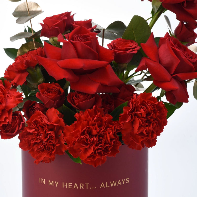 Vibrant red roses and carnations in deep burgundy vase with gold "In My Heart... Always" text.