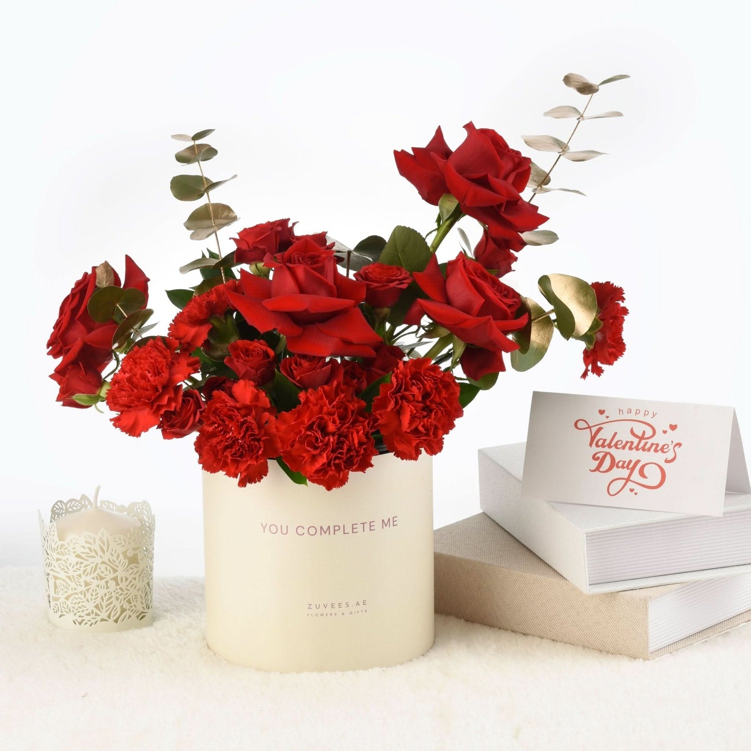 Vibrant red roses and carnations in cream cylinder with "You Complete Me" message.