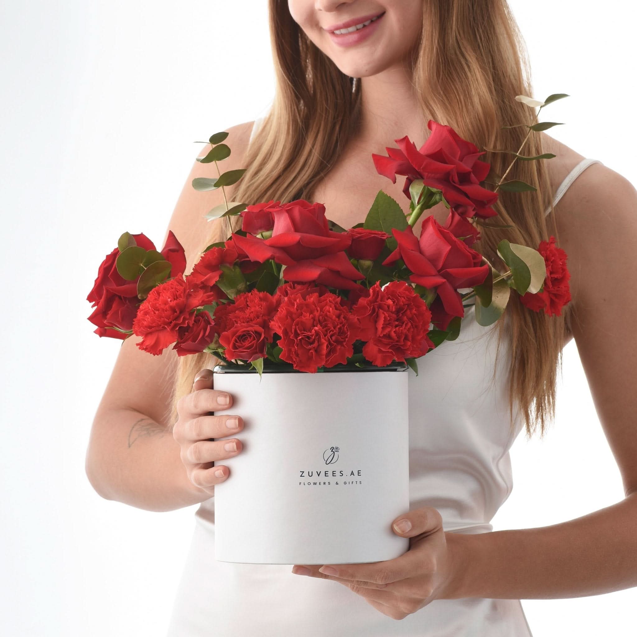 Woman holds white box of vibrant red roses and carnations, elegant gift presentation.