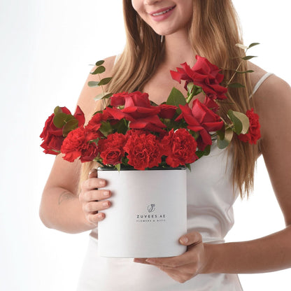 Woman holds white box of vibrant red roses and carnations, elegant gift presentation.