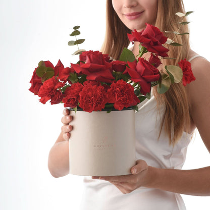 Elegant white box holds vibrant red roses and carnations, accented with eucalyptus.