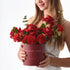 Woman holds deep red rose and carnation bouquet in matte burgundy box with gold "In My Heart... Always" inscription.