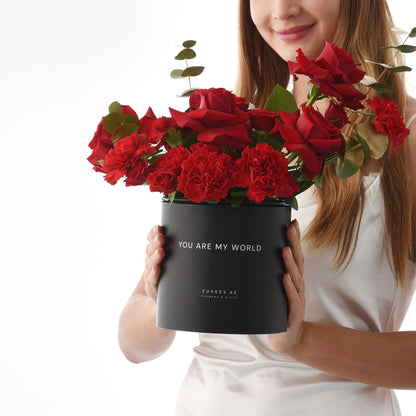 Black box holds vibrant red roses and carnations, with "You Are My World" message.