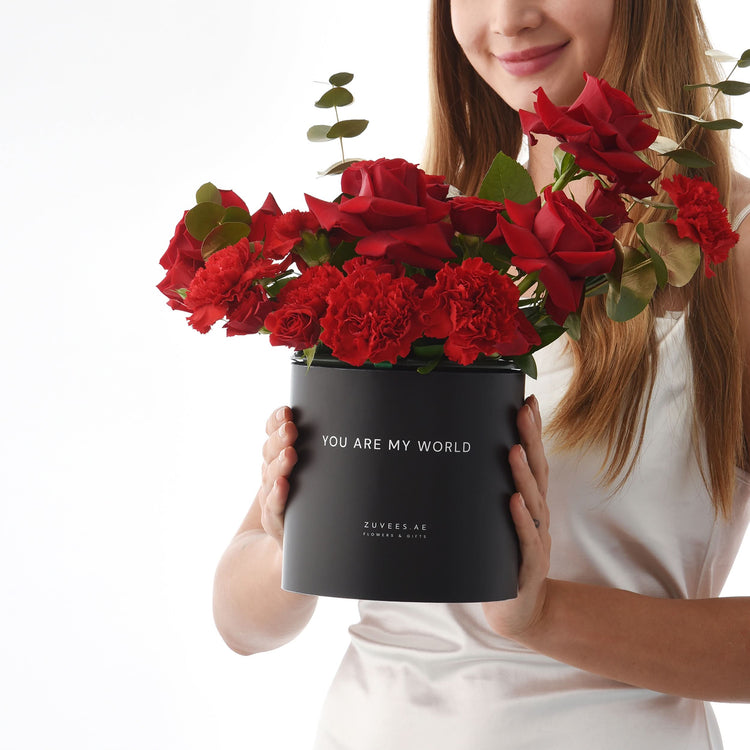 Black box holds vibrant red roses and carnations, with "You Are My World" message.