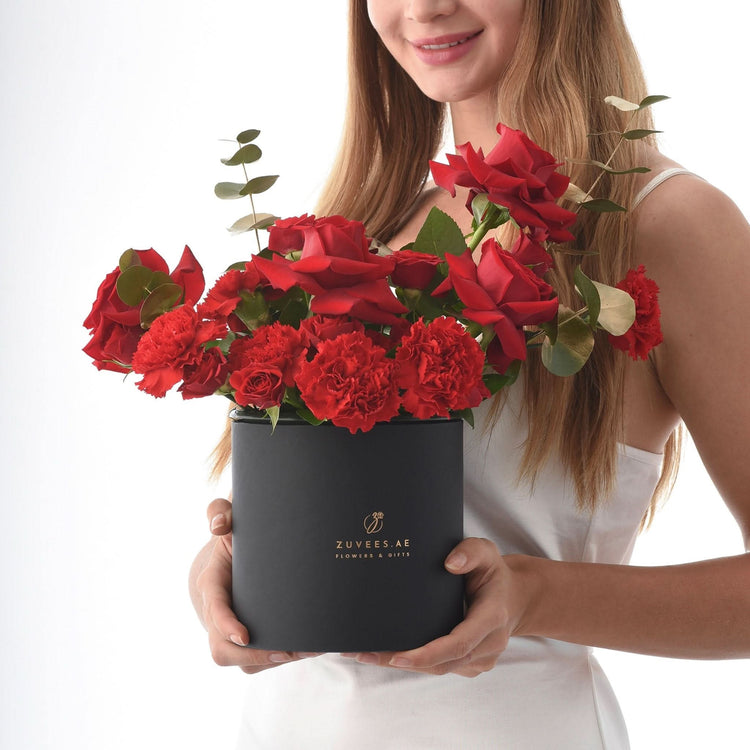 Woman holds black box overflowing with vibrant red roses and carnations.