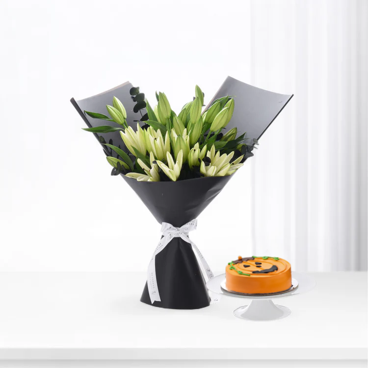 Elegant white lilies in black wrap, beside festive orange pumpkin cake on white stand.