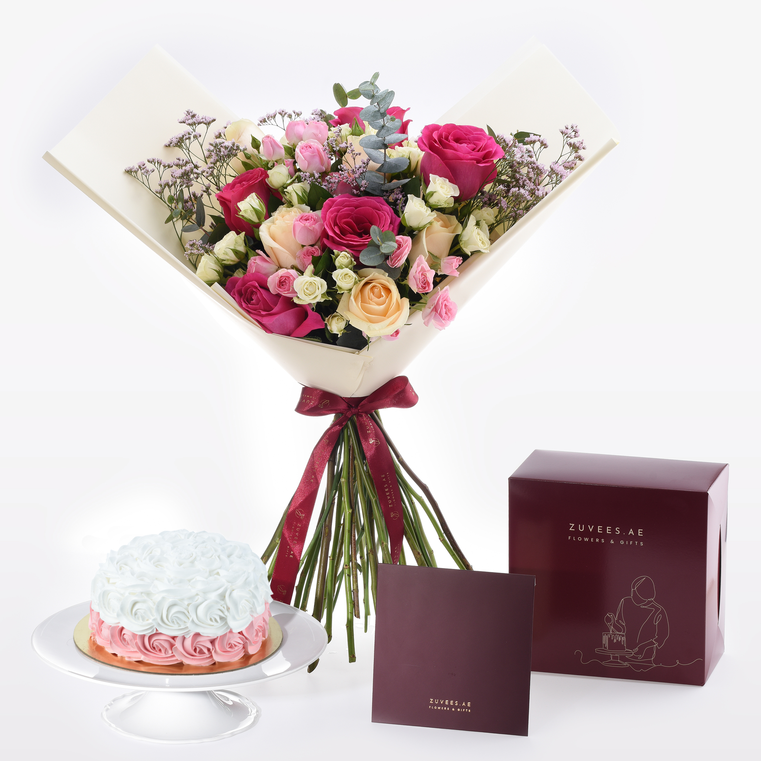 Vibrant pink, peach, and white roses with baby’s breath, elegantly wrapped in cream paper and burgundy ribbon, paired with a rose-iced cake and branded gift box.