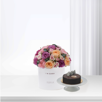 White box holds vibrant pink, purple, peach roses beside chocolate cake.