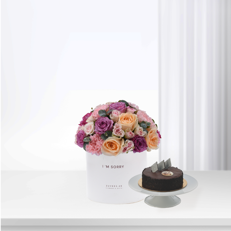White box holds vibrant pink, purple, peach roses beside chocolate cake.