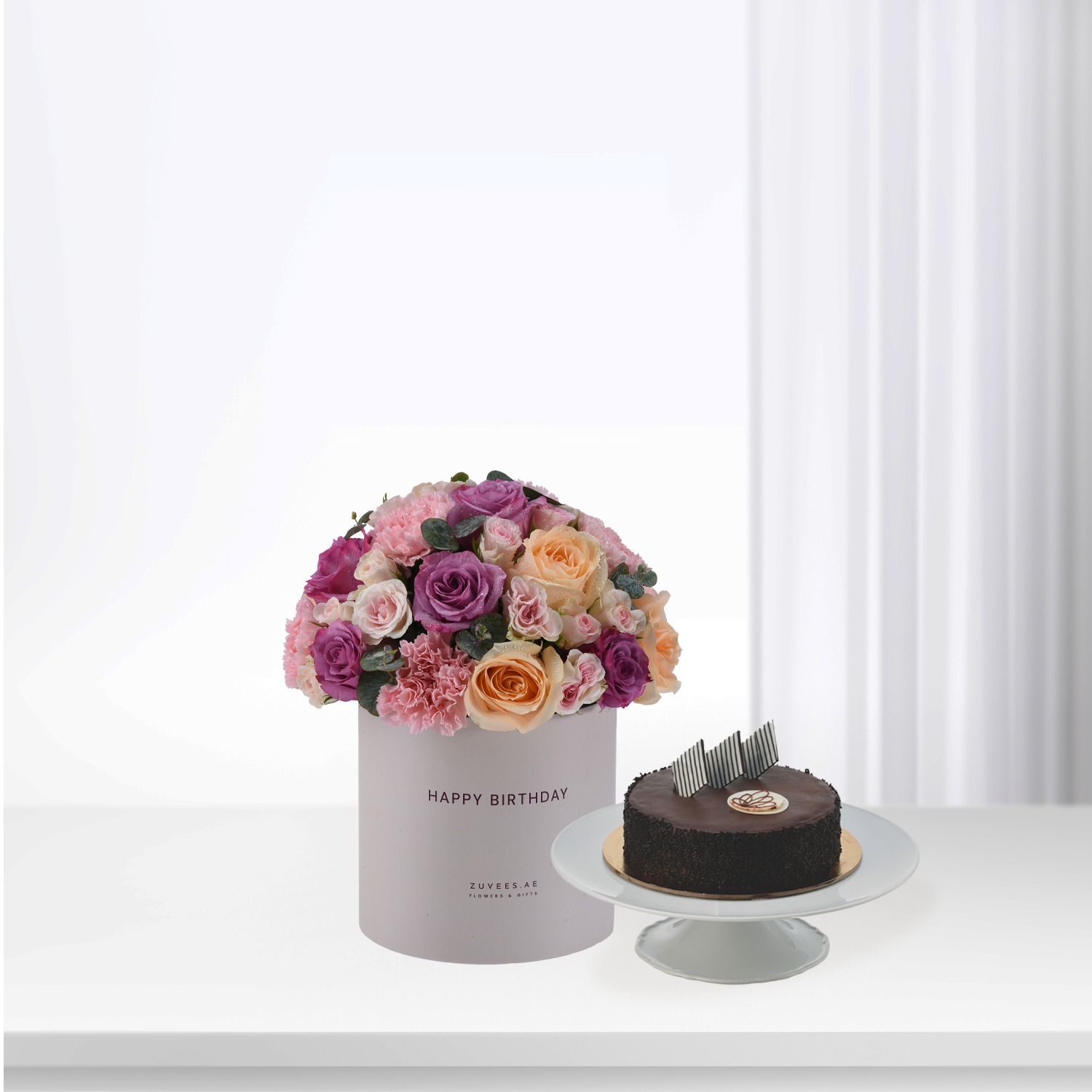 Pastel pink, purple, and peach roses in box beside chocolate cake.
