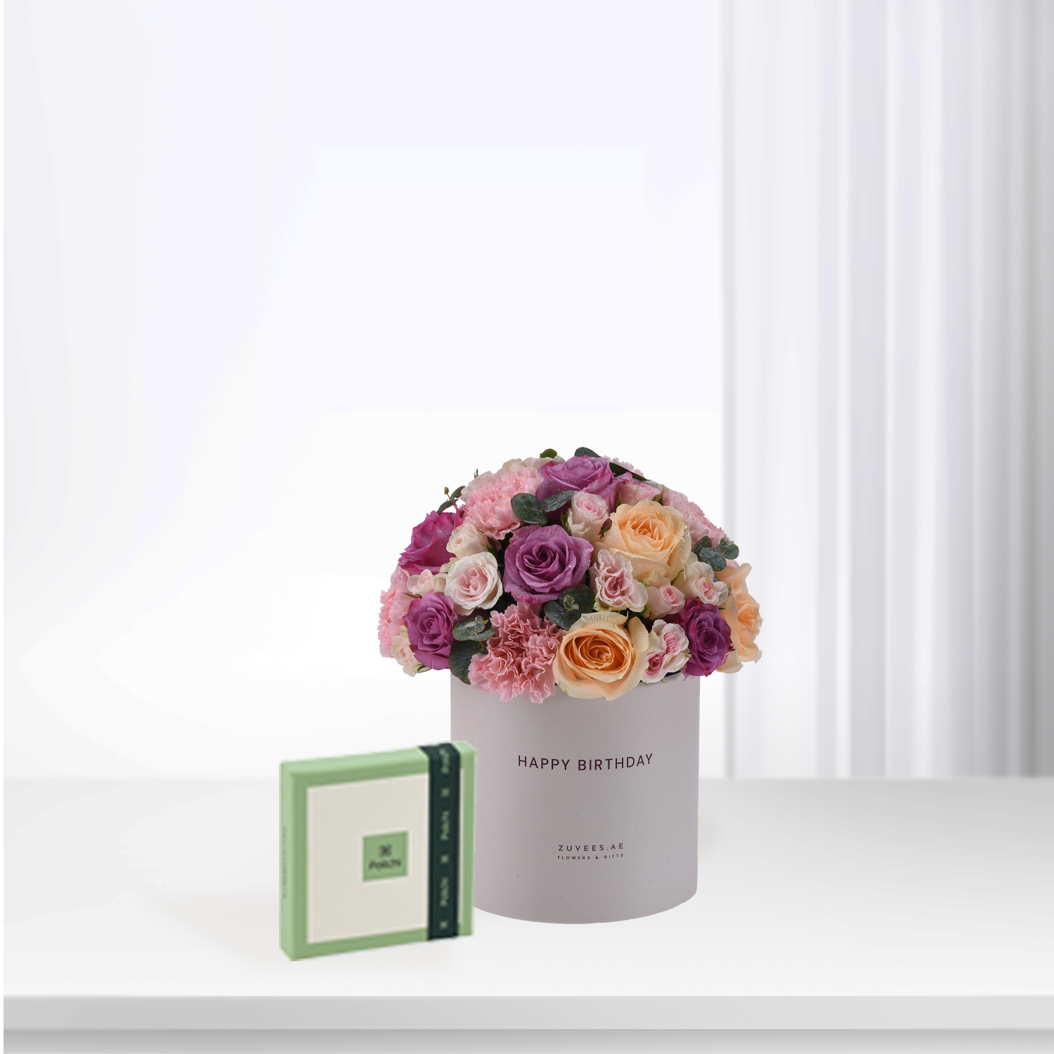 Pastel pink, purple, and peach roses in a "Happy Birthday" box with green chocolate gift.