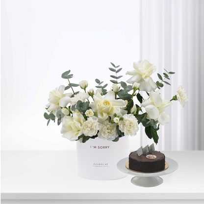 White roses and eucalyptus in minimalist vase beside chocolate cake.