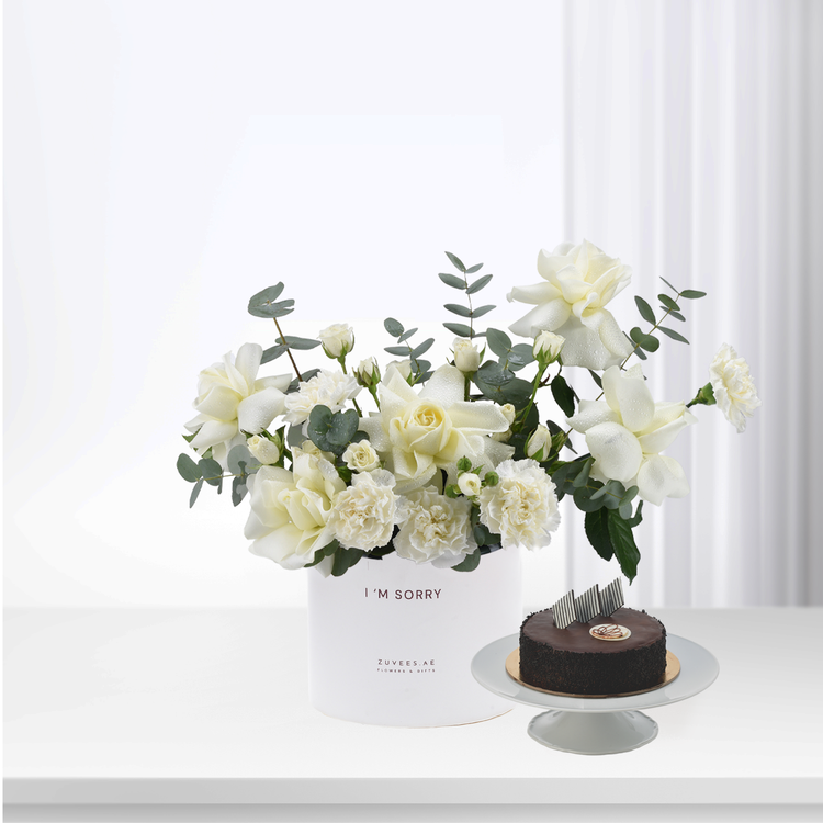 White roses and eucalyptus in minimalist vase beside chocolate cake.