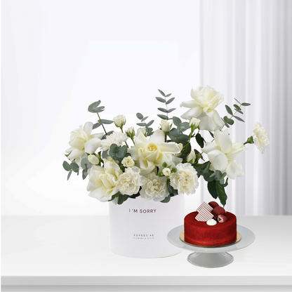 White roses and eucalyptus in minimalist box beside red velvet cake.