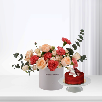 Pink roses and carnations in white box beside red velvet cake.