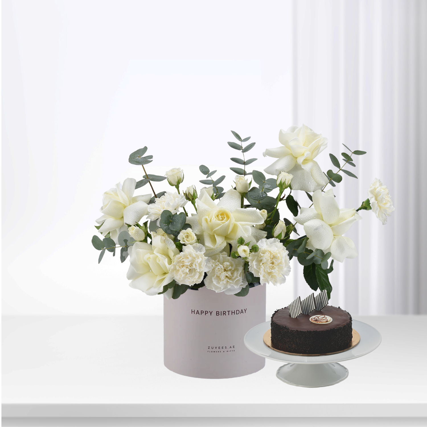 Elegant white roses and eucalyptus in pastel box, beside chocolate cake.