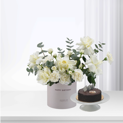 Elegant white roses and eucalyptus in pastel box, beside chocolate cake.