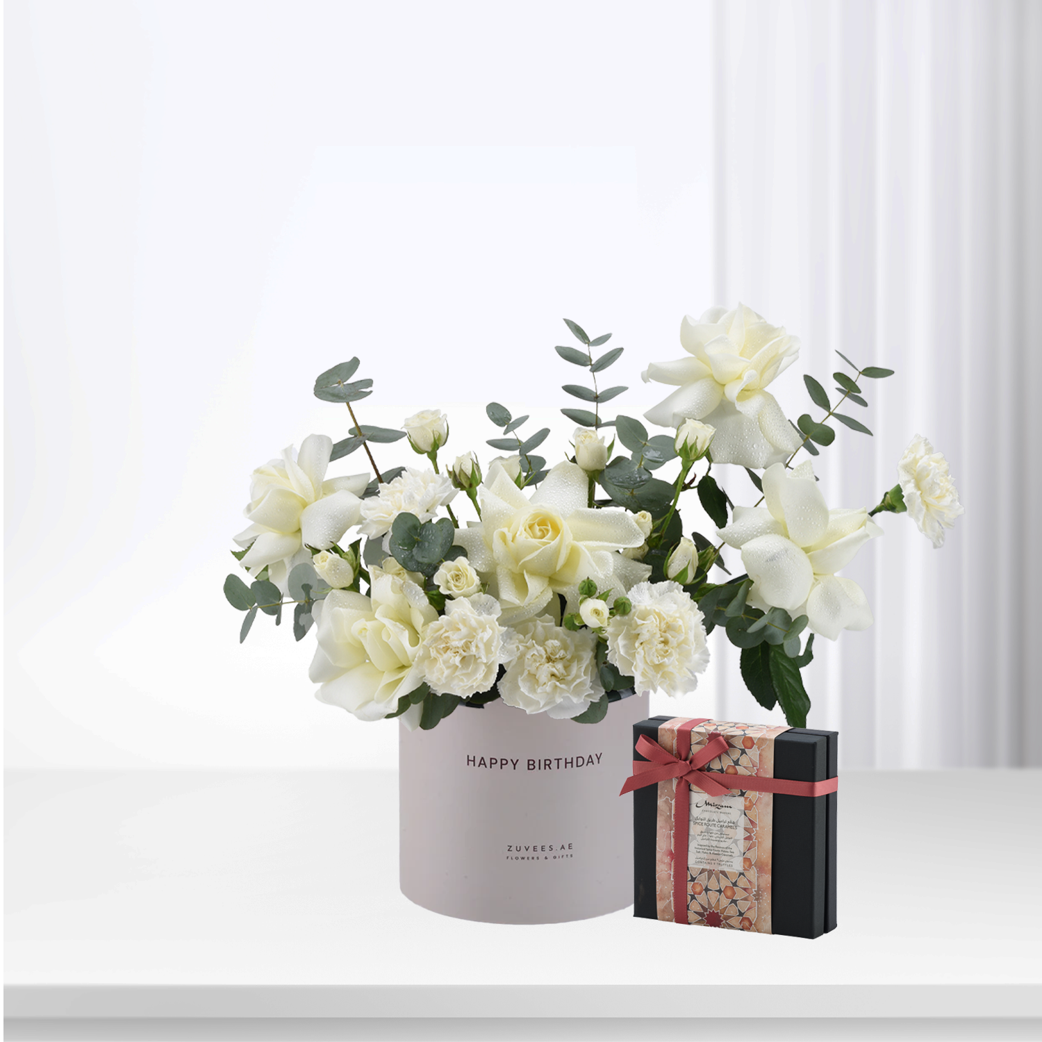 White roses and eucalyptus in "Happy Birthday" box with chocolate gift.