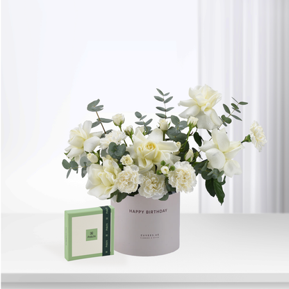Elegant white roses and eucalyptus in pastel cylinder, "Happy Birthday" gift set beside Patchi chocolate box.