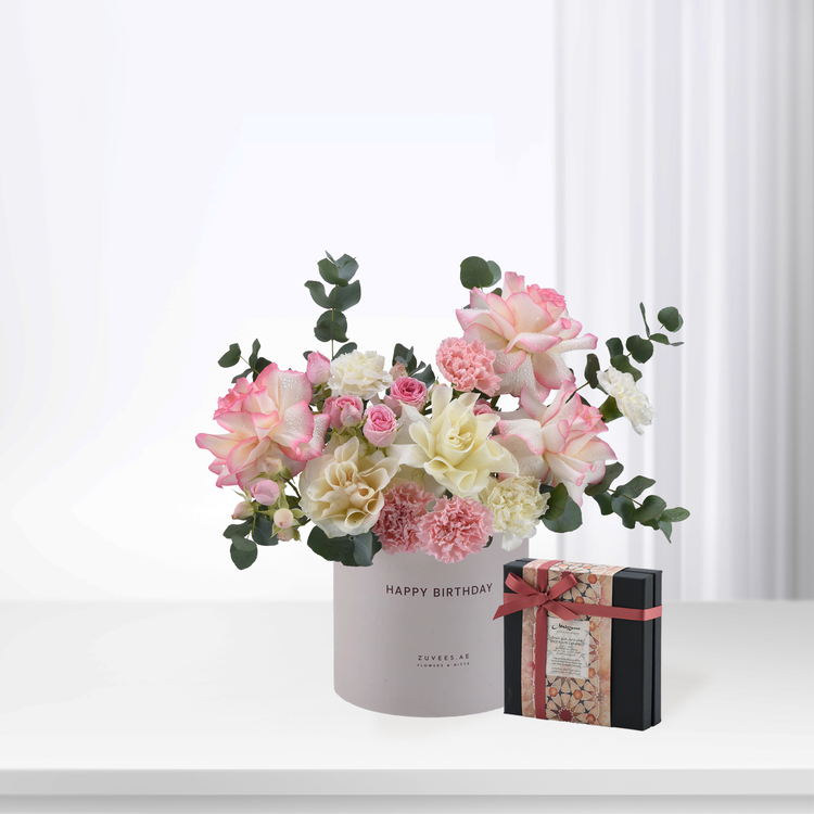 Soft pink and white roses with eucalyptus in branded box, beside decorative gift.