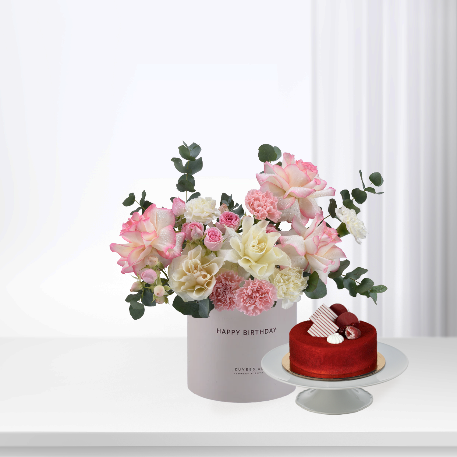 Pastel pink and white roses with eucalyptus, beside red velvet cake.
