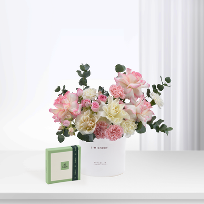 Soft pink and cream roses with eucalyptus in white vase, beside green Patchi box.