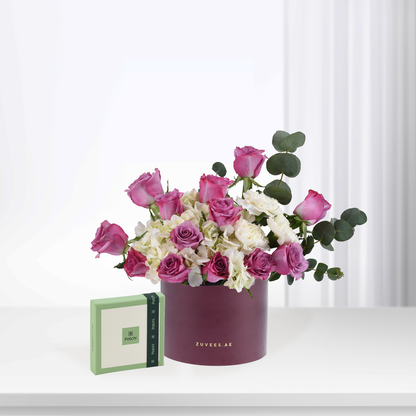 Elegant burgundy hat box filled with pink roses and white hydrangeas, beside green Patchi chocolate box.