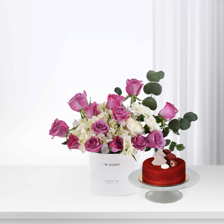 Pink roses and white hydrangeas in white box beside red velvet cake.