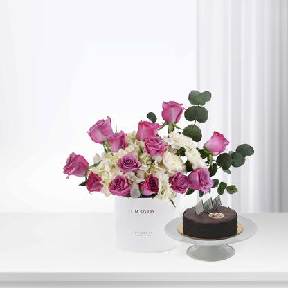 Pink roses and white hydrangeas in white box beside chocolate cake.