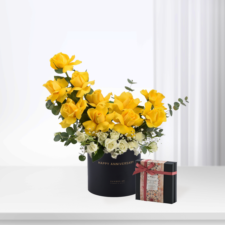 Vibrant yellow roses with white accents in black "Happy Anniversary" box, beside elegant gift box.