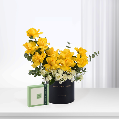 Vibrant yellow roses with white accents in black "Happy Anniversary" box, paired with green Patchi chocolate gift.