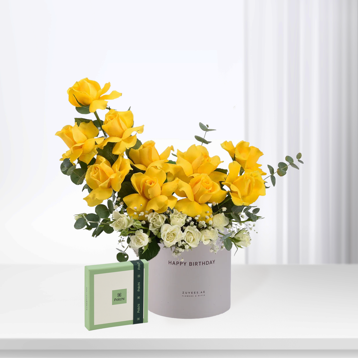 Vibrant yellow roses with white accents in gray "Happy Birthday" vase, beside green Patchi box.
