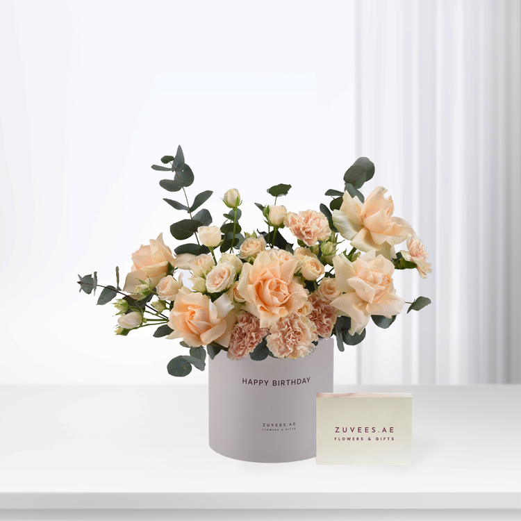 Soft peach roses and carnations in white cylinder with "Happy Birthday" text.
