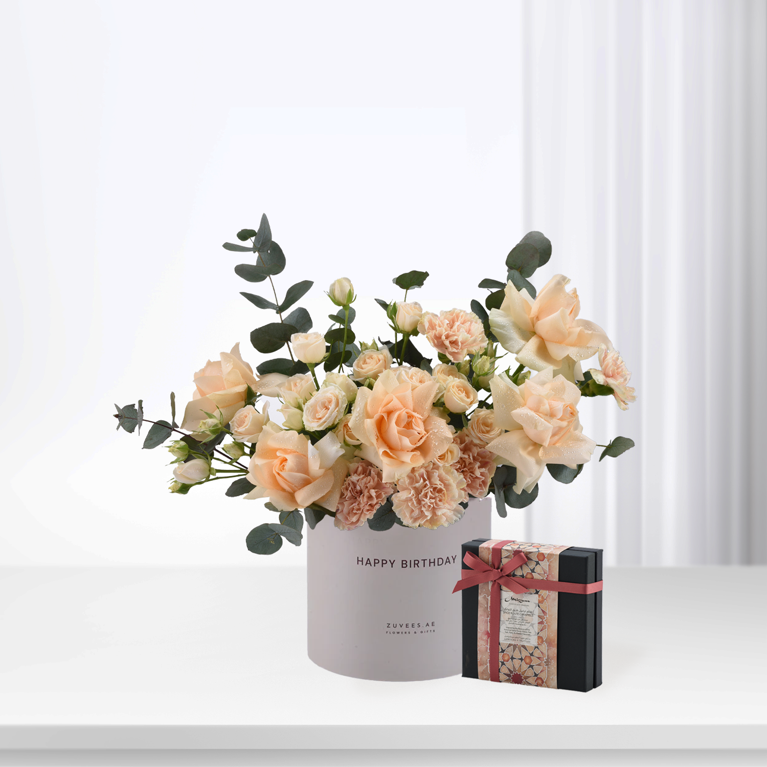 Soft peach roses and eucalyptus in white "Happy Birthday" vase with chocolate gift box.