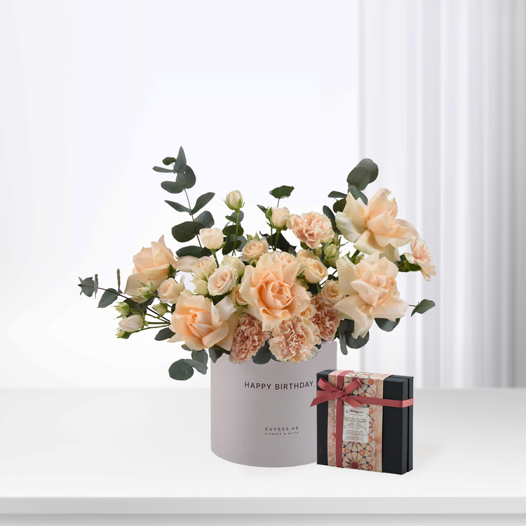 Soft peach roses and eucalyptus in white "Happy Birthday" vase with chocolate gift box.