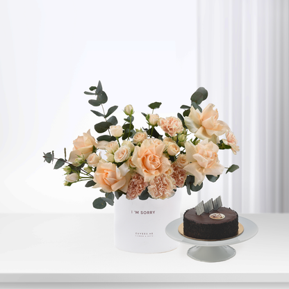 Soft peach roses and eucalyptus in white vase beside chocolate cake.