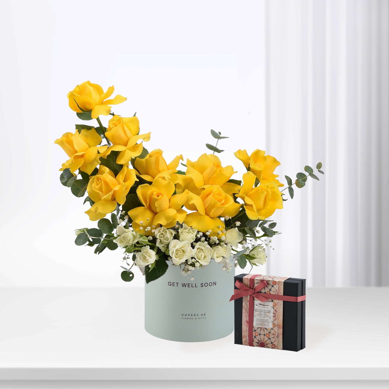 Vibrant yellow roses in mint cylinder with "Get Well Soon" text, beside patterned gift box.