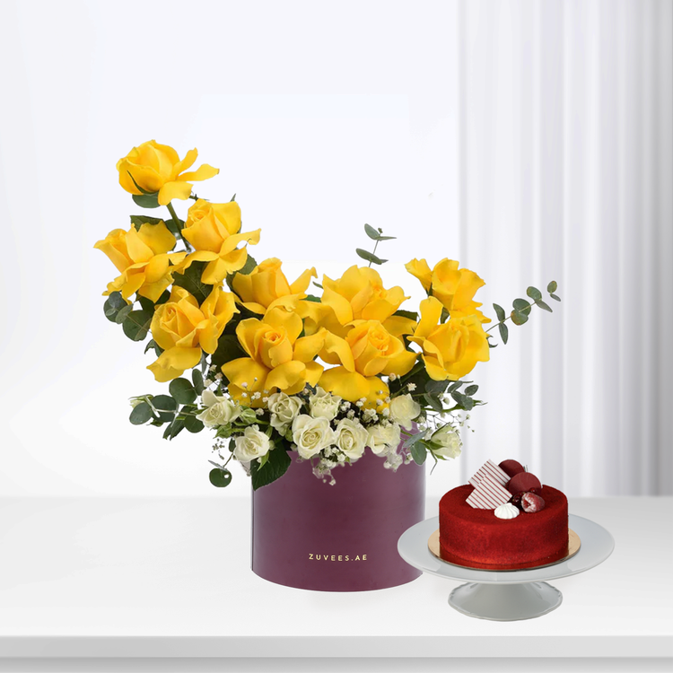 Vibrant yellow roses and white blooms in purple box beside red velvet cake.