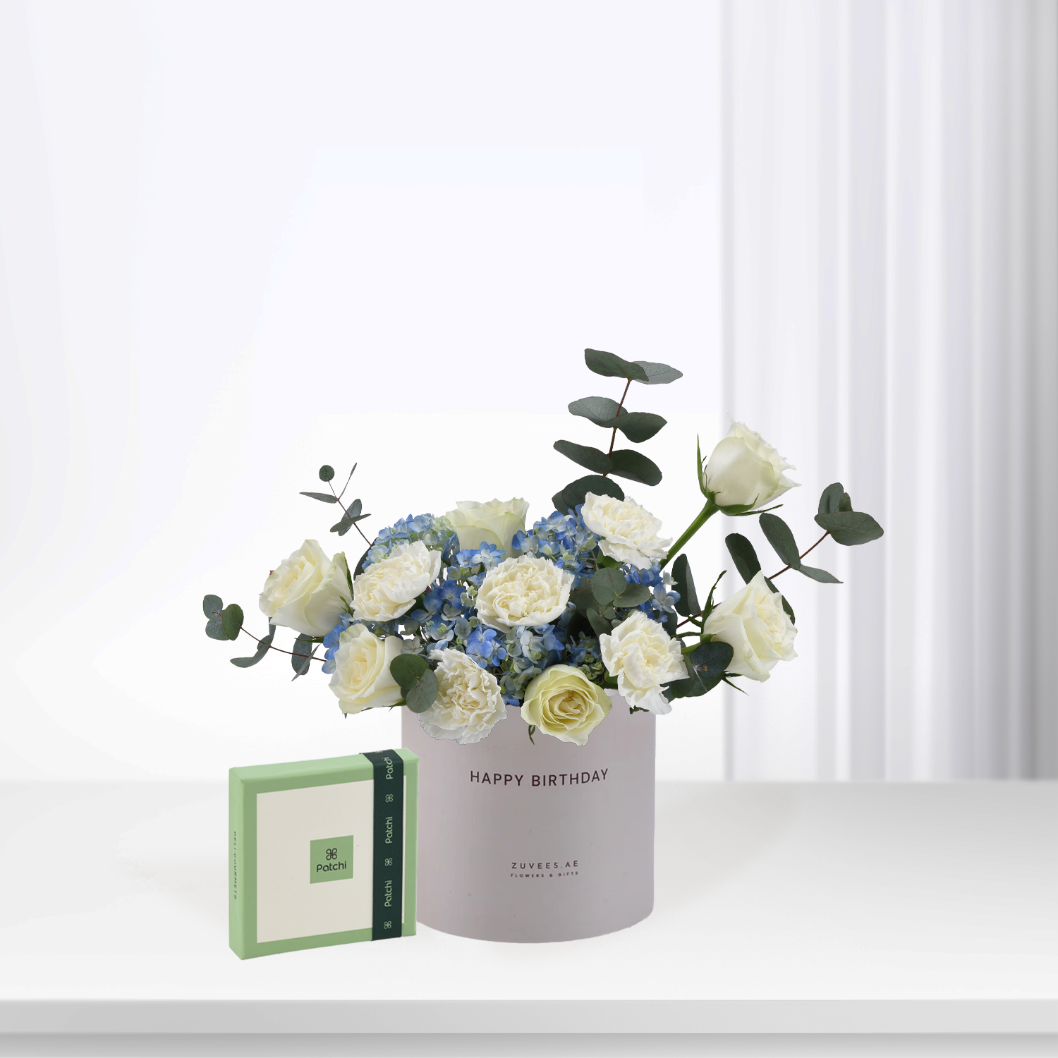 Elegant white roses and blue hydrangeas in gray "Happy Birthday" box with green Patchi soap.