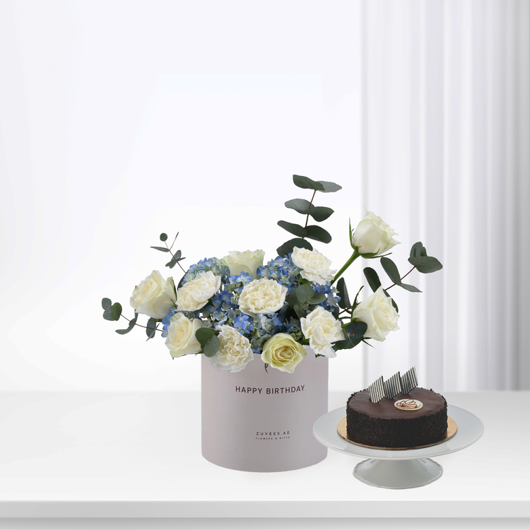 Elegant white roses and blue hydrangeas in pastel box beside chocolate cake.