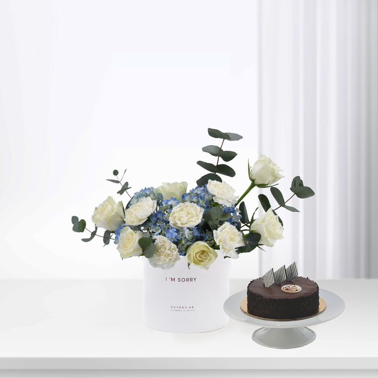 White roses and blue hydrangeas in minimalist vase beside chocolate cake.