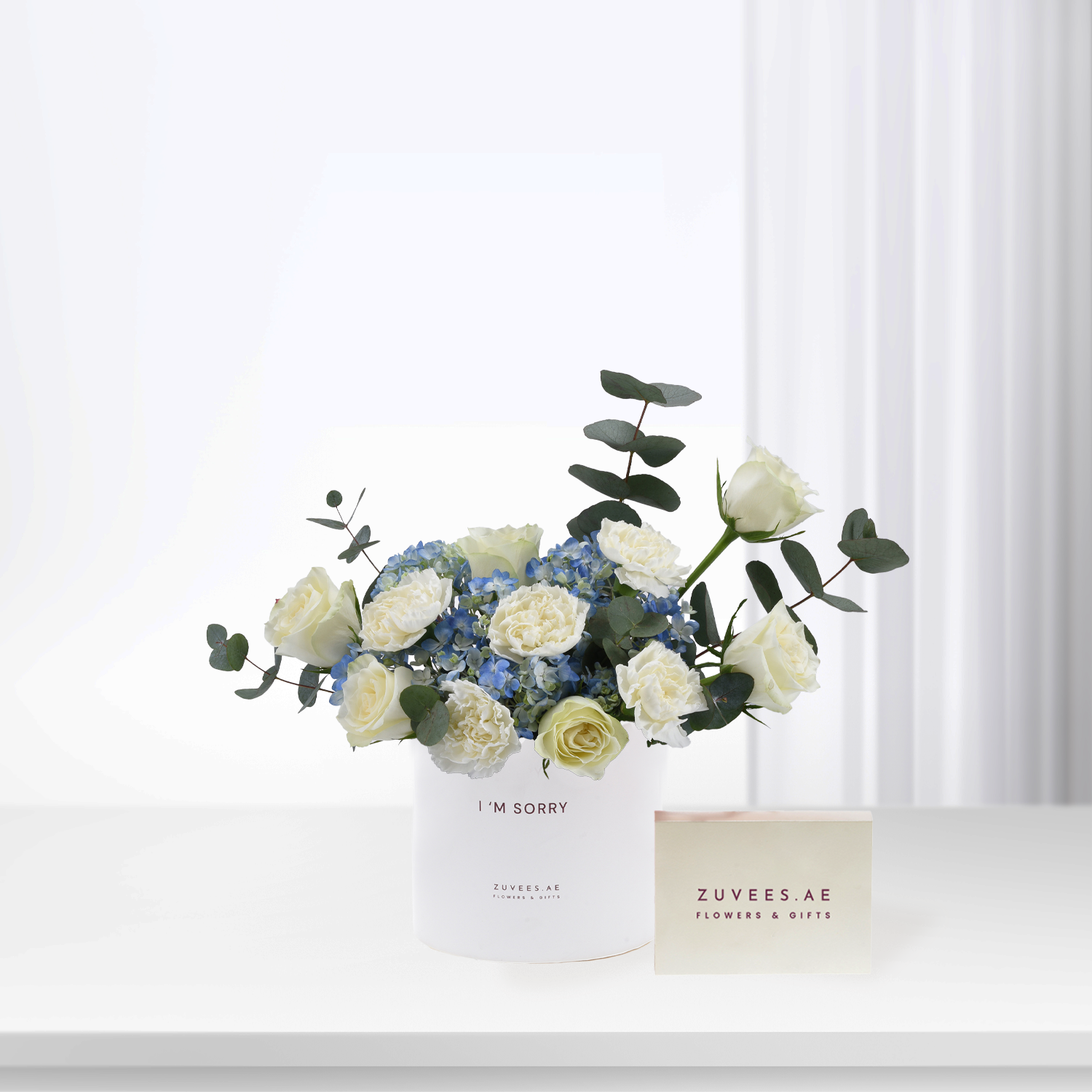 White roses and blue hydrangeas in minimalist white vase with "I&