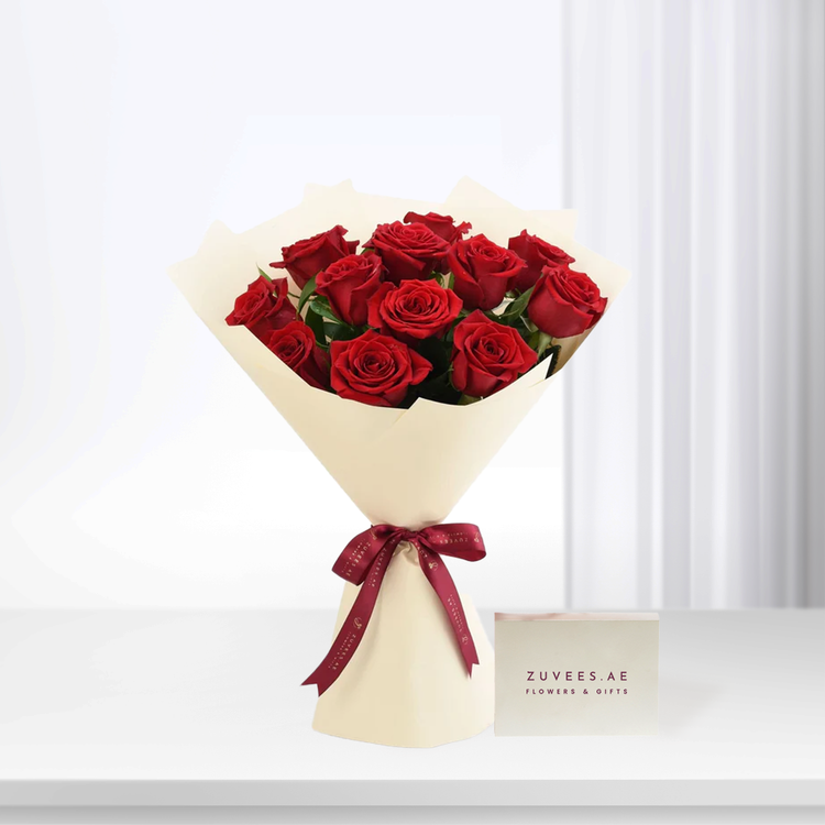 Vibrant red roses in cream wrap, burgundy ribbon, Zuvees.AE card, minimalist white background.