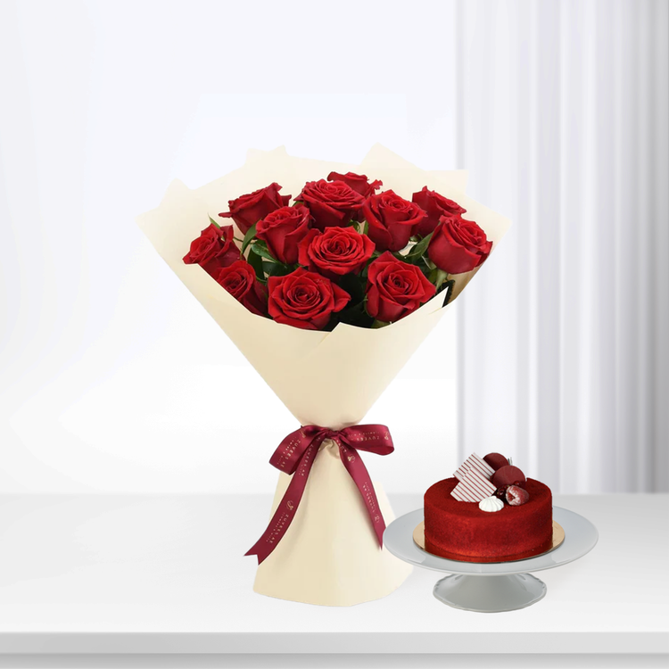 Vibrant red roses in cream wrap with burgundy bow, beside red velvet cake on stand.