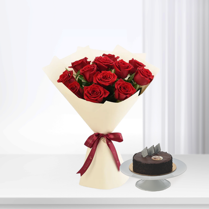 Vibrant red roses in cream wrap with burgundy ribbon, beside chocolate cake on stand.