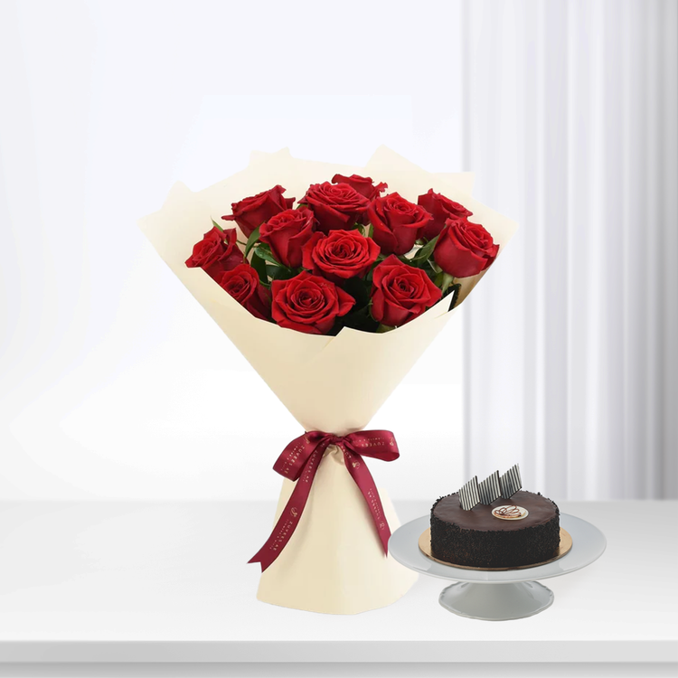 Vibrant red roses in cream wrap with burgundy ribbon, beside chocolate cake on stand.