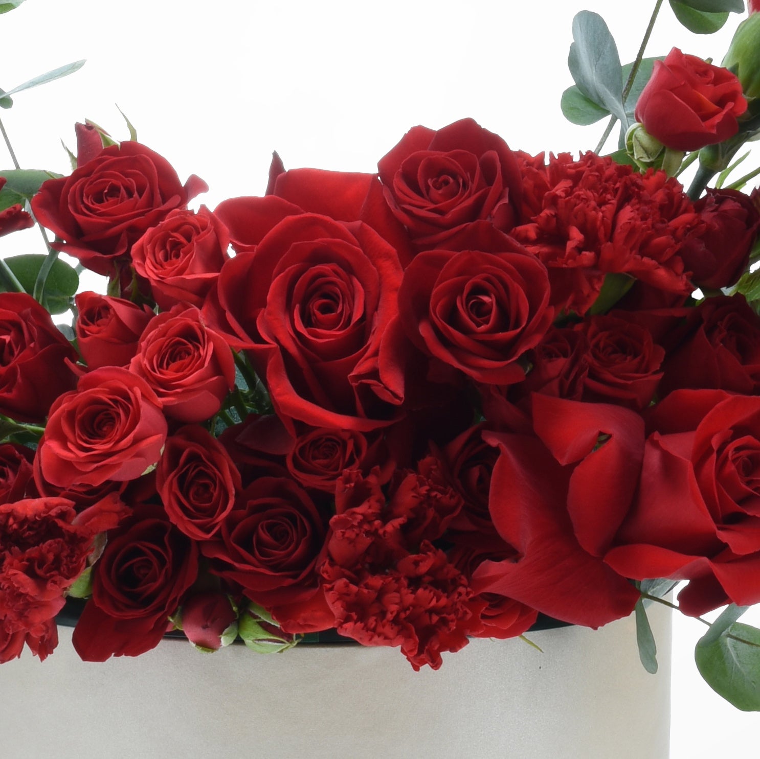 Vibrant red roses and carnations in lush, romantic bouquet with green foliage accents.